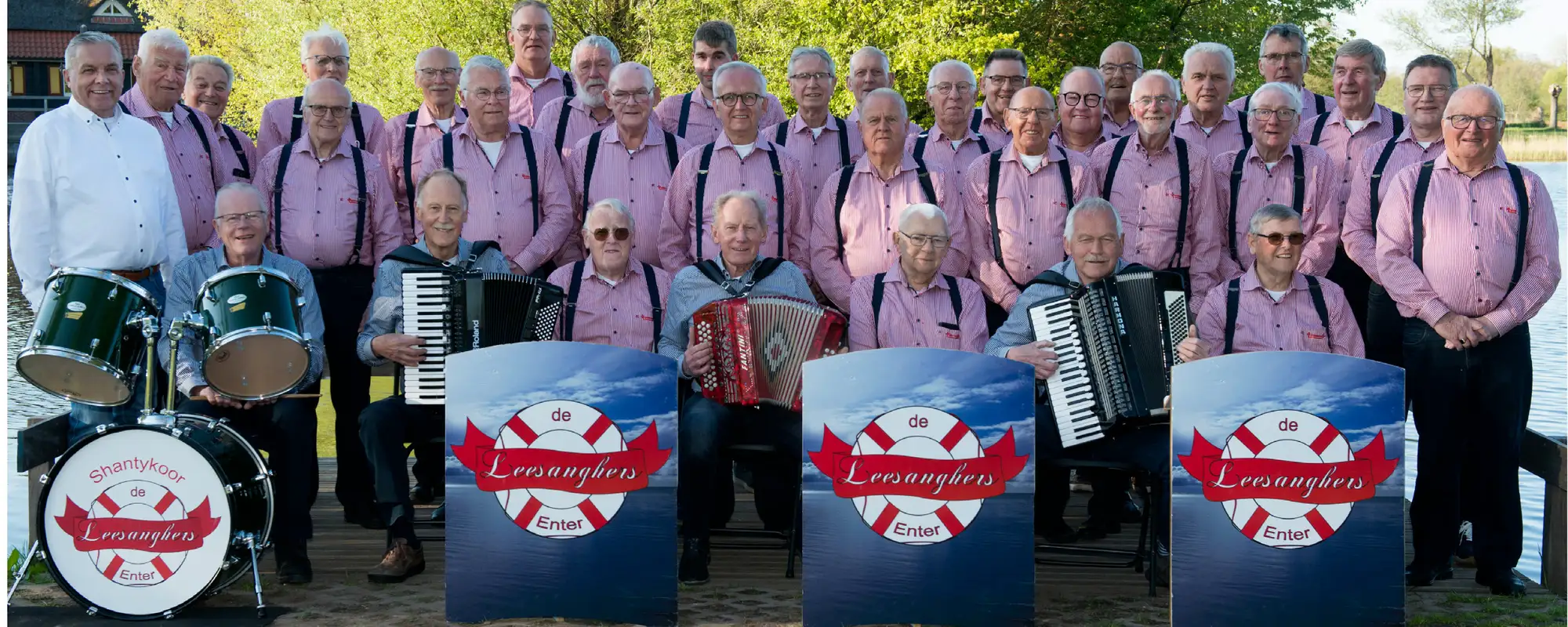 De Leesanghers in rood-wit gestreepte overhemden, met accordeons en drumstel, aan het water bij Enter